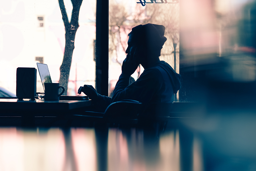 shadowy image of a man at a cafe looking at a comouter