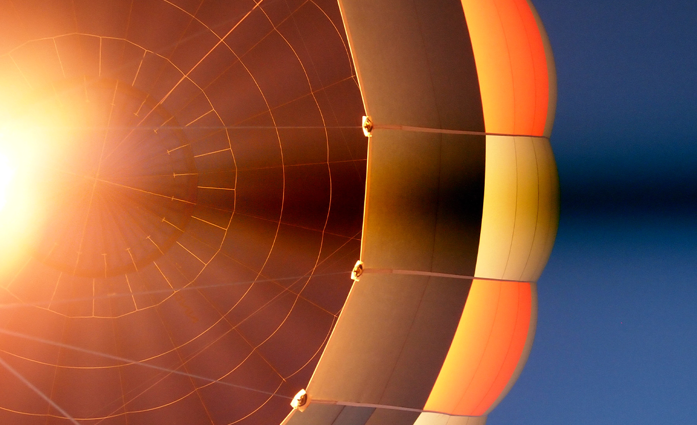 upward view of light shining through an orange hot air balloon against a blue sky
