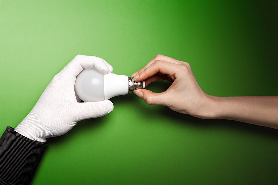 white glove and hand hold a lightbulb green background